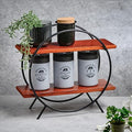 Orbit Duo Shelf by Metallics Home featuring two wooden shelves in a circular metal frame, displaying jars labeled Coffee, Sug