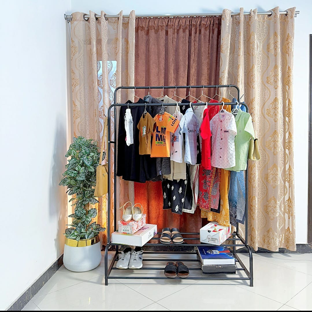 Dual Pole Metal Clothes Stand by Metallics Home featuring clothes on hangers, dual shoe tiers, and a decorative plant.