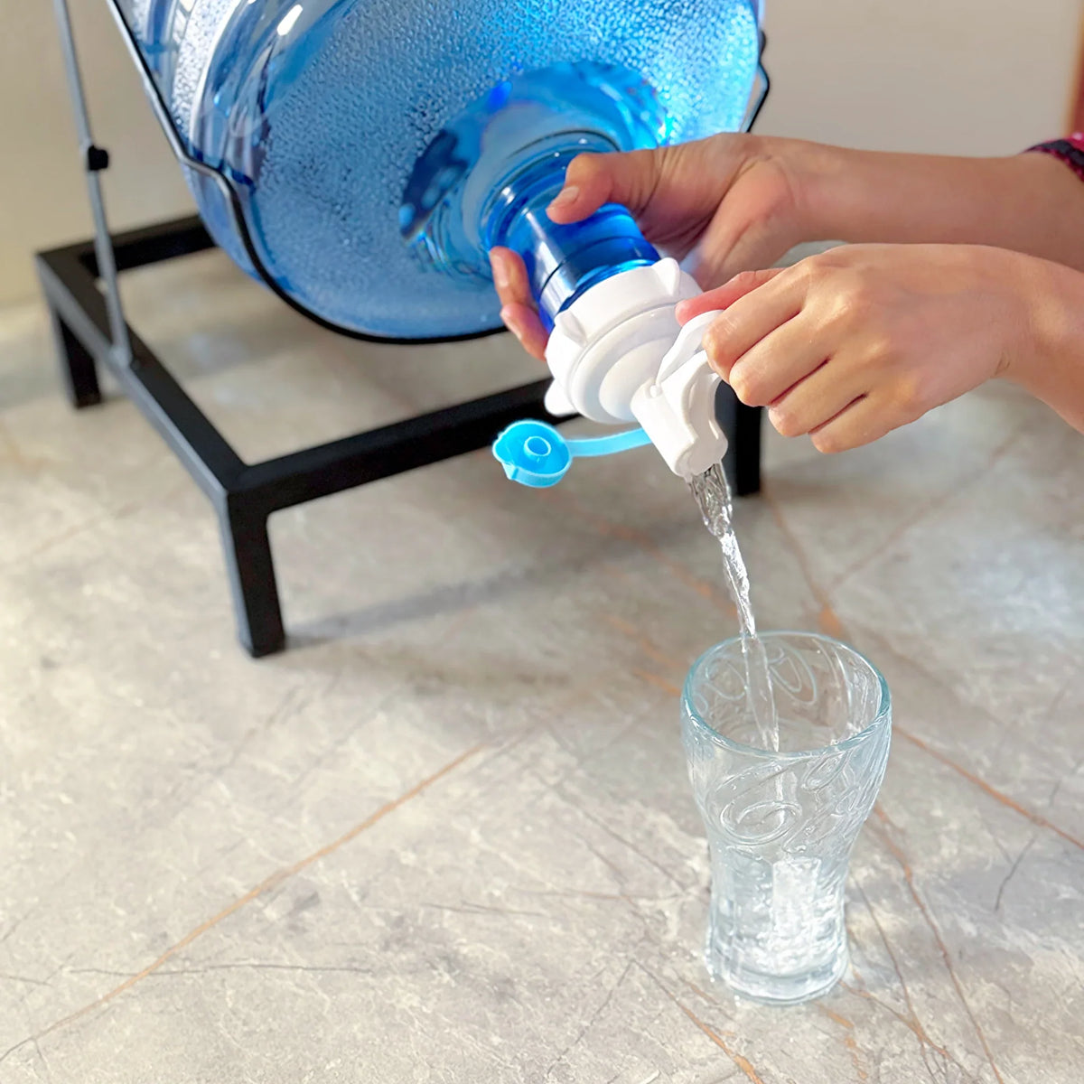 Swinging Bottle Rack by Metallics Home, featuring a person pouring water from a large blue bottle into a glass.