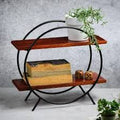 Orbit Duo Shelf by Metallics Home features two wooden shelves supported by a circular black metal frame, with decorative plan